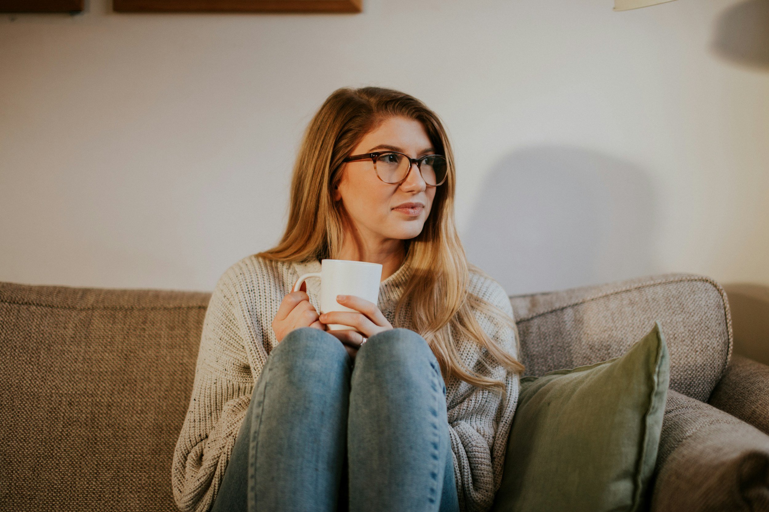 Woman sitting on a sofa holding a mug, reflecting, representing someone considering EMDR therapy for anxiety or emotional healing.