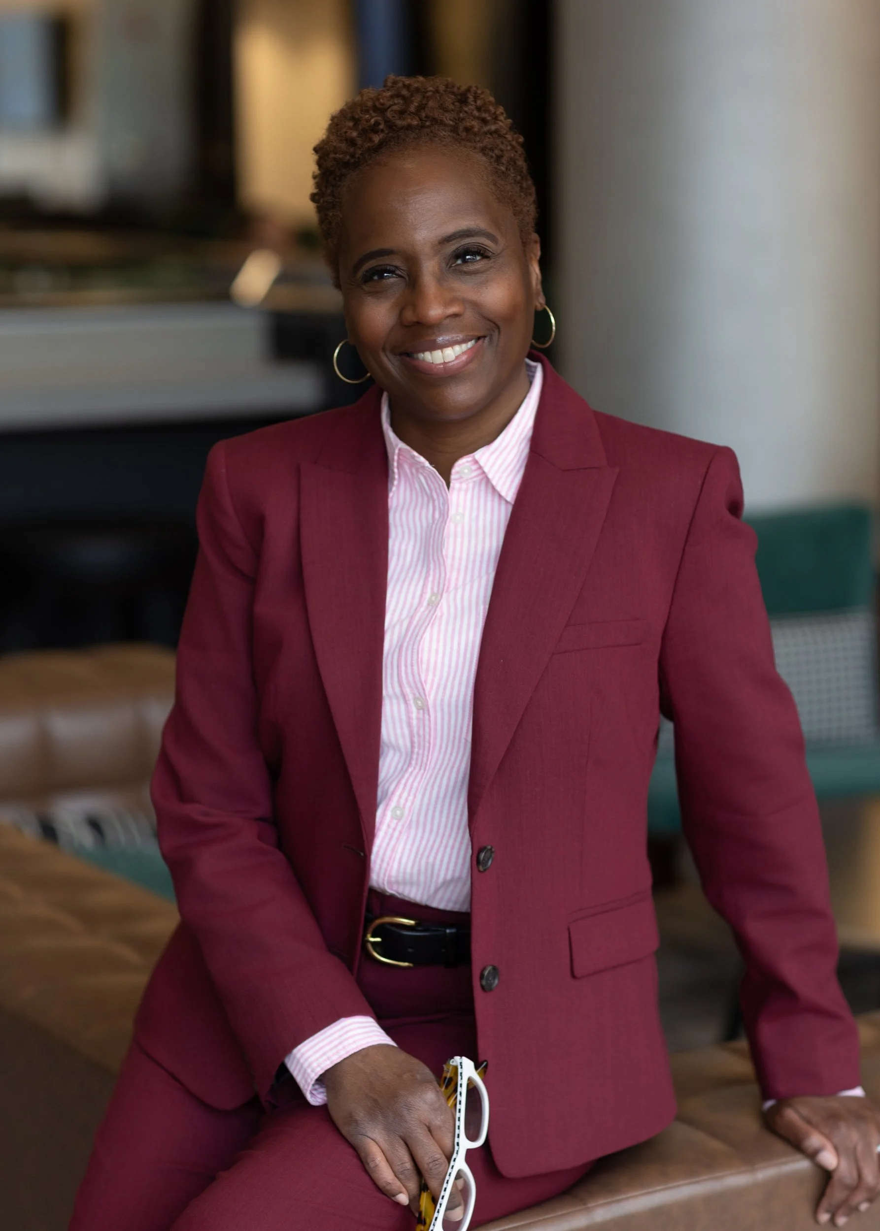 business woman in burgundy suit smiling with glasses in her hand.