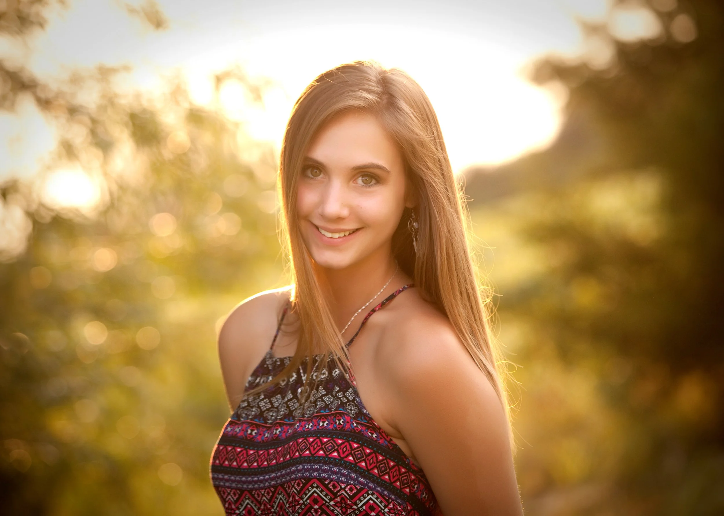 outdoor portrait of senior girl with trees and the sun in the background