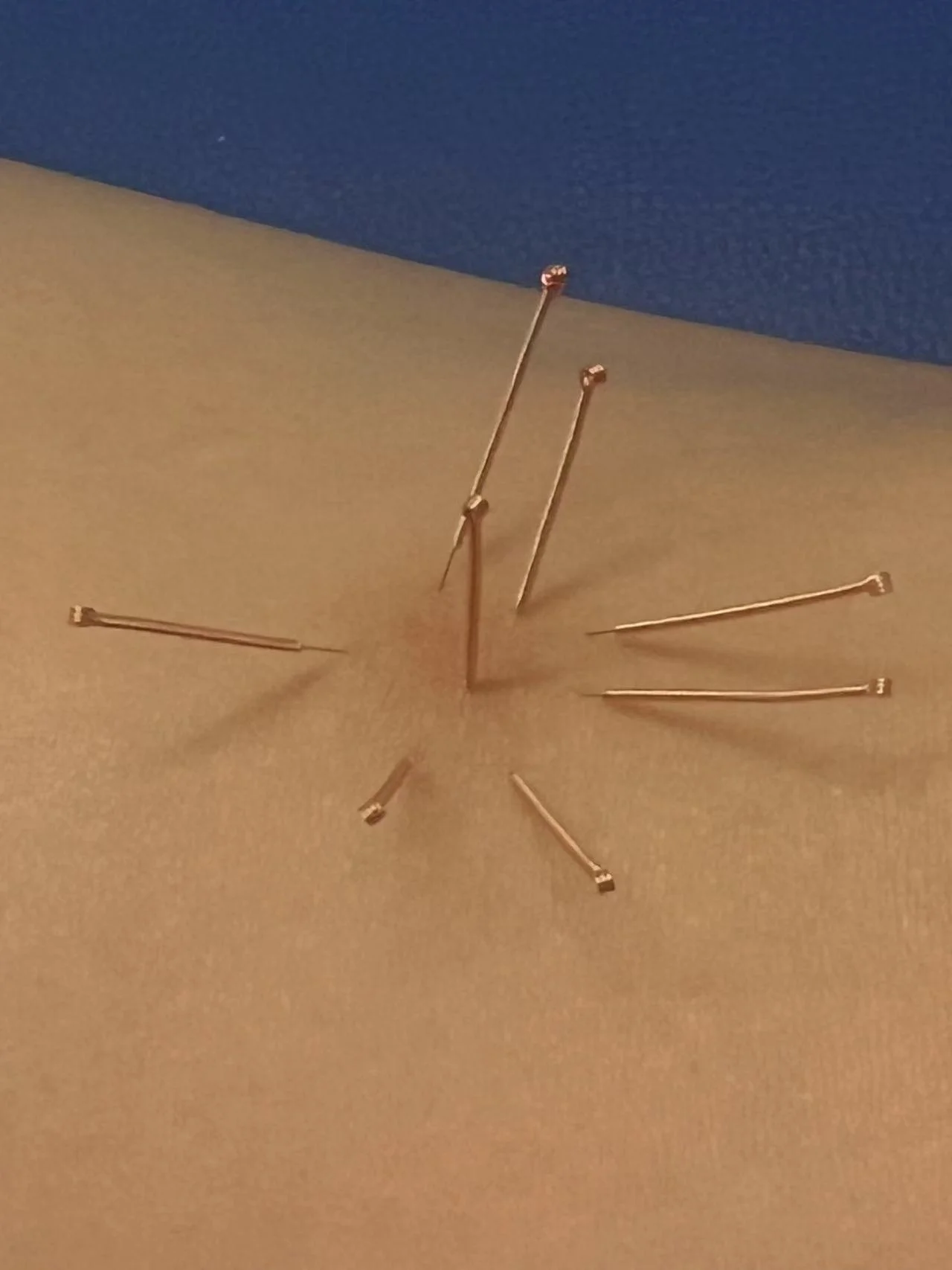 A clock with no numbers, made with gold-colored sewing pins on a beige and blue background.