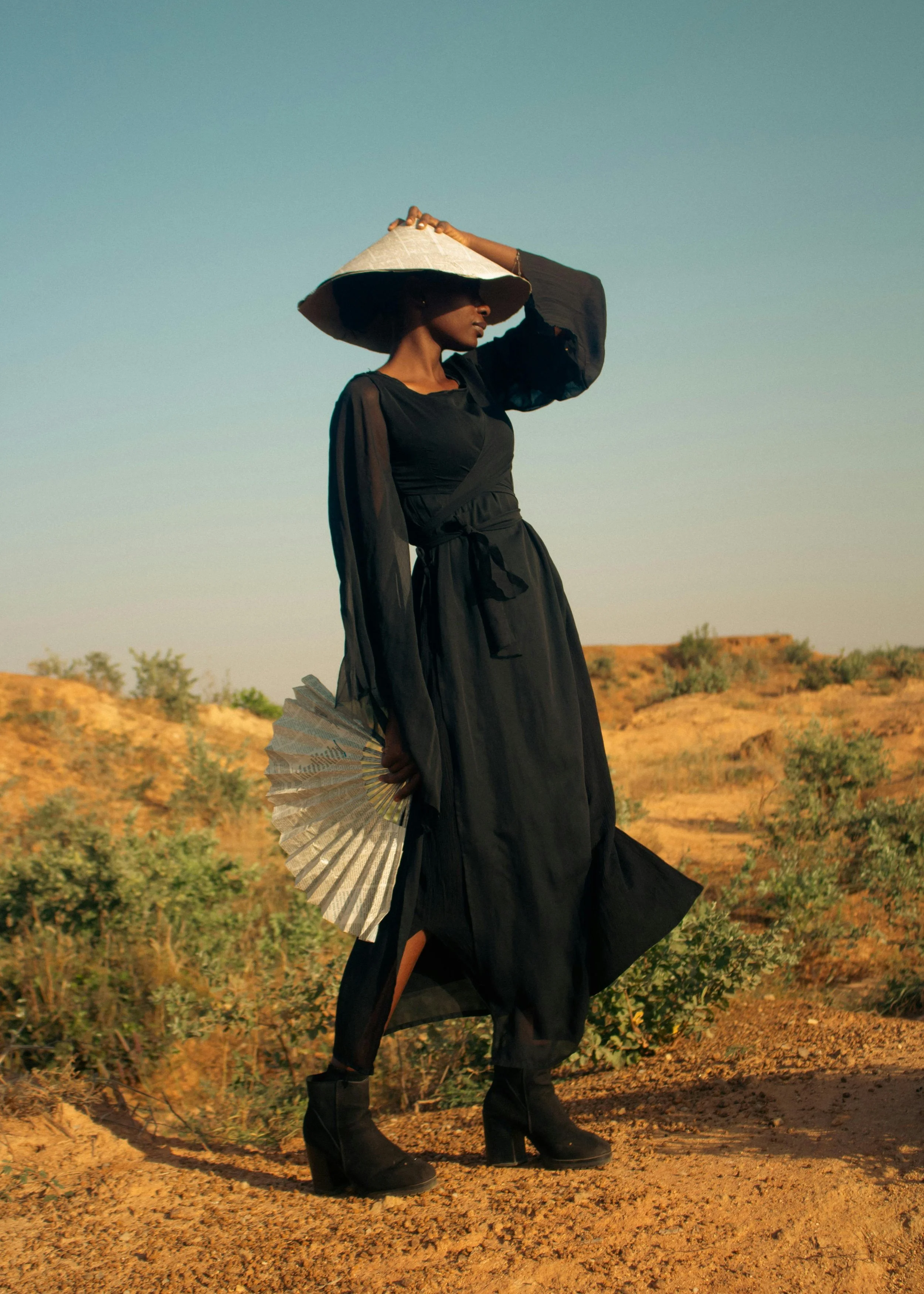 african american woman in a black dress with a silver triangular had and silver fan expanded in her hand in the desert