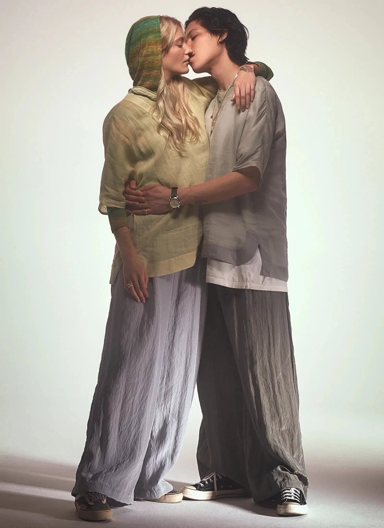 A man and woman are standing close, about to kiss, with their arms around each other against a plain background.