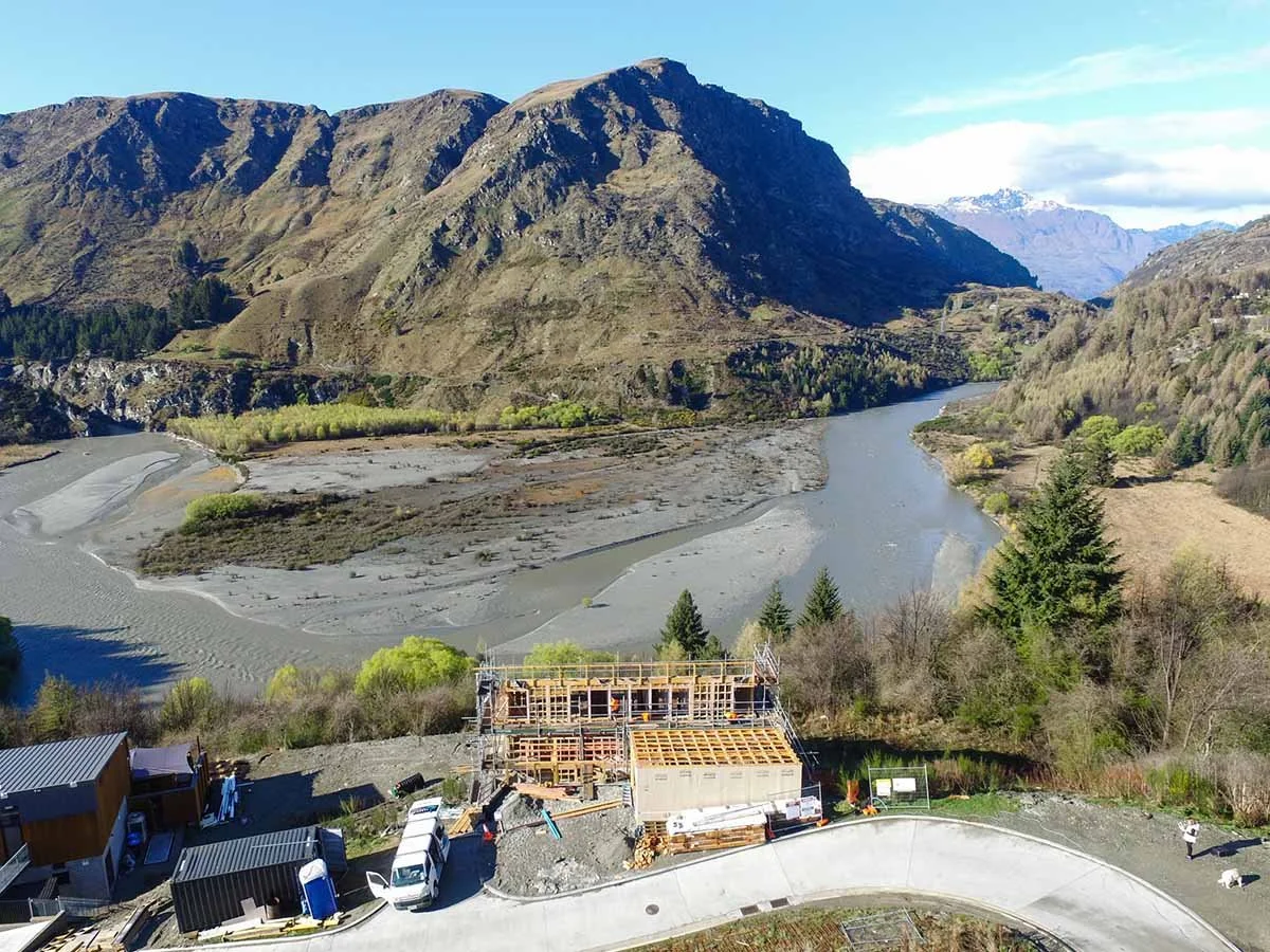 Scaffolding and home under construction in from of a river and mountain