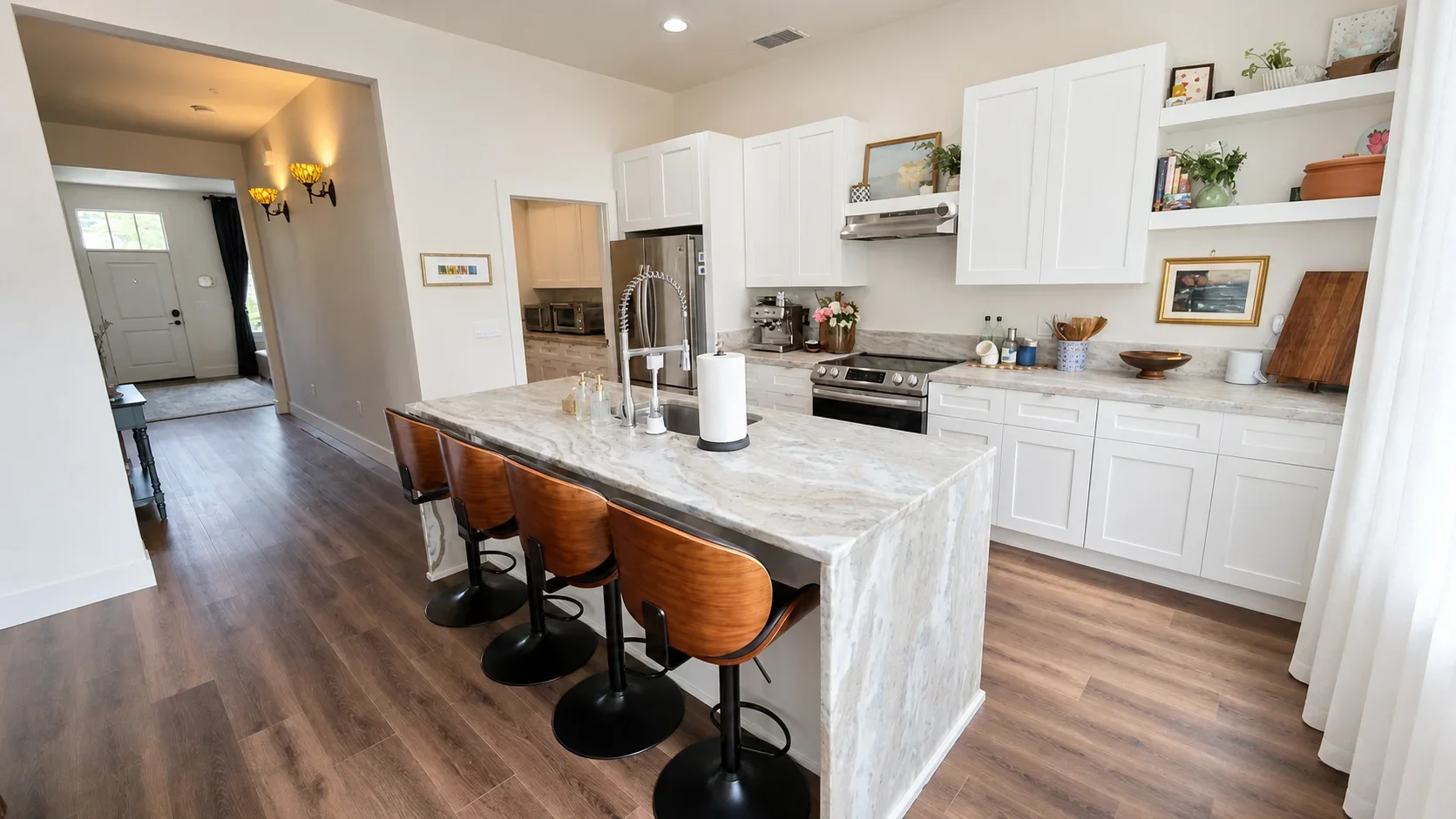 Modern kitchen with white cabinets, marble island with three brown barstools, stainless steel appliances, open shelves with decorative items, and hardwood floors.