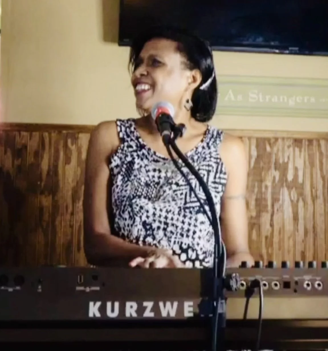 A woman singing or speaking into a microphone while playing a Kurzweil keyboard.