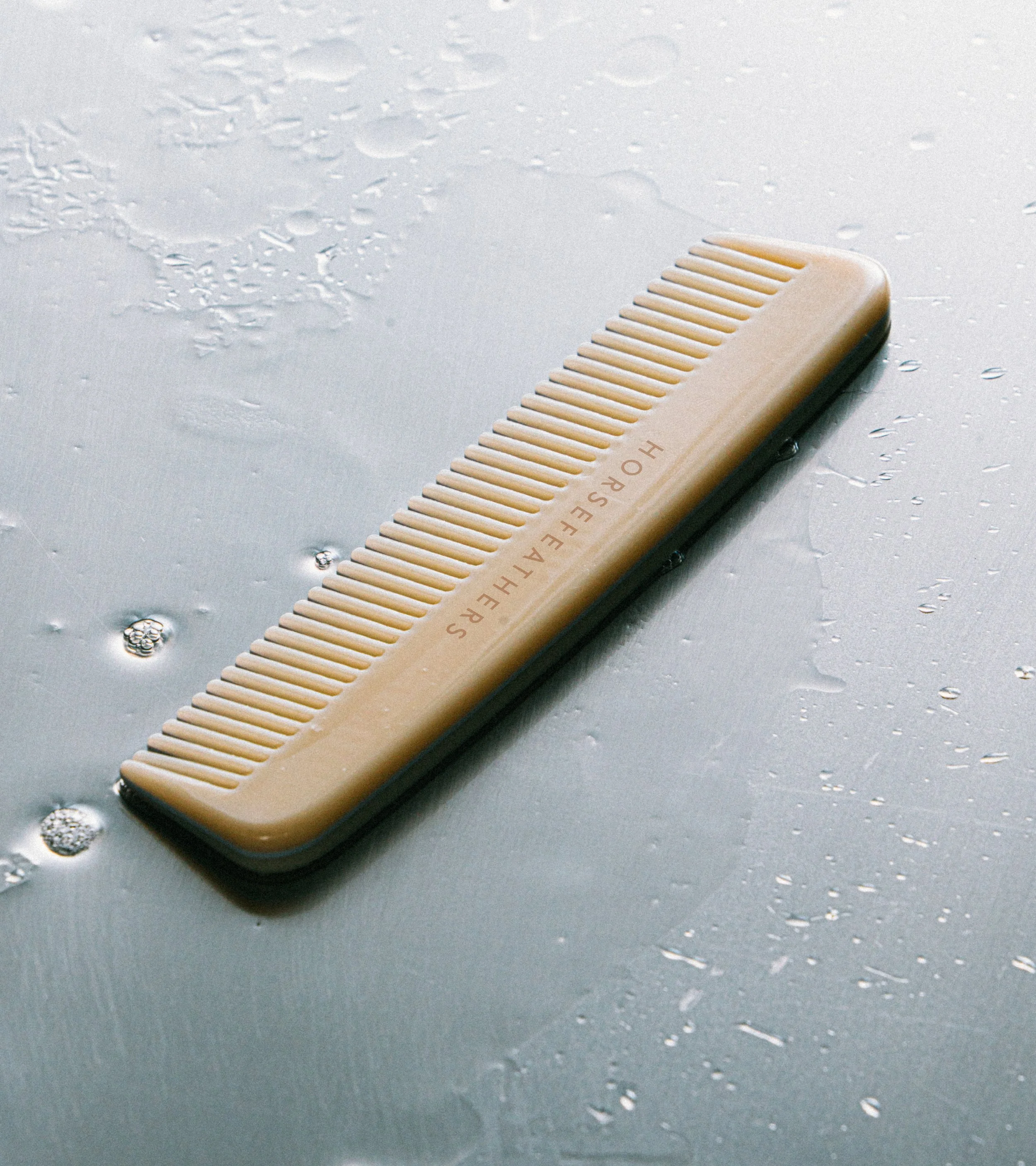 A beige hairbrush with black edges lying on a wet, dark gray surface.