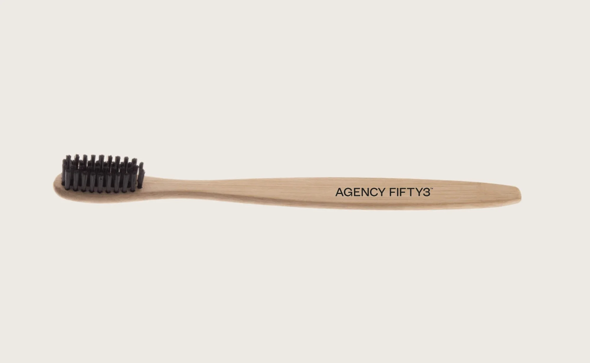 A wooden toothbrush with black bristles and words 'AGENCY FIFTY3' printed on the handle.