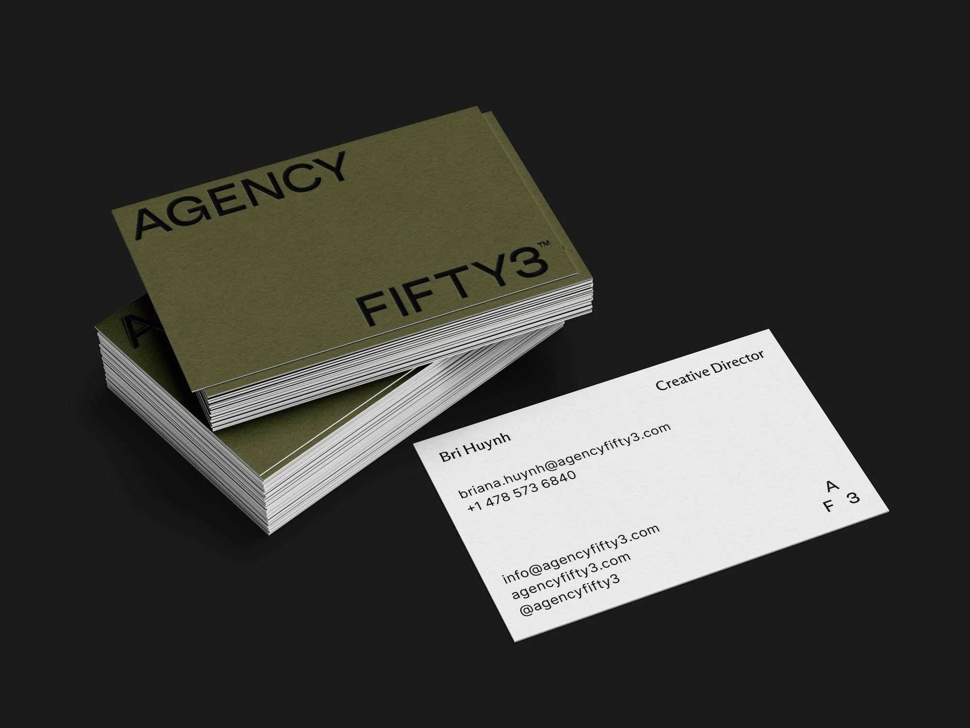 Stack of business cards for Agency Fifty3 with a black background, showing a white card with contact details and titles, and dark green cards with black text.