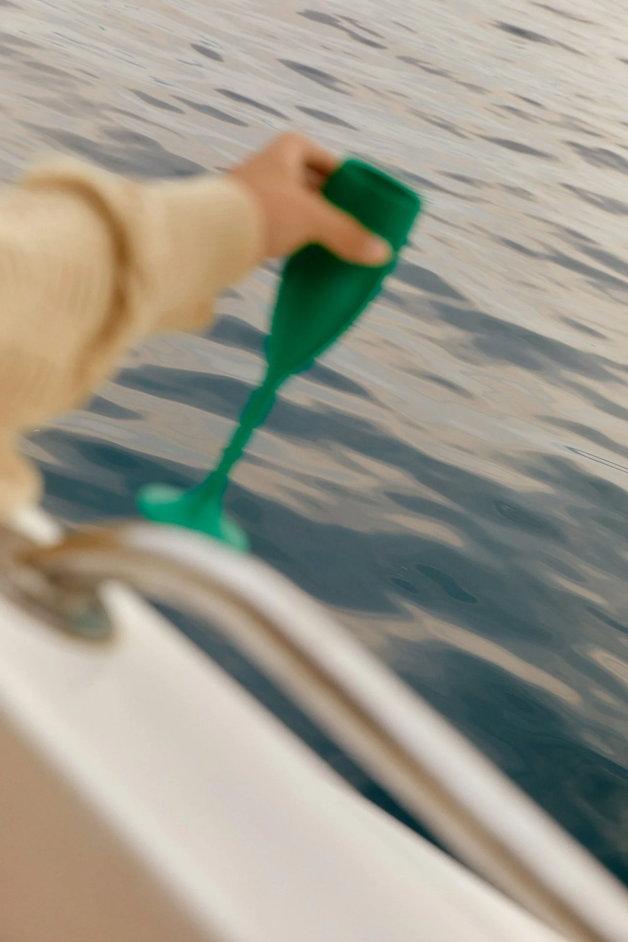 A hand holding a green object over water on a boat, with the boat's edge and railing visible in the foreground.