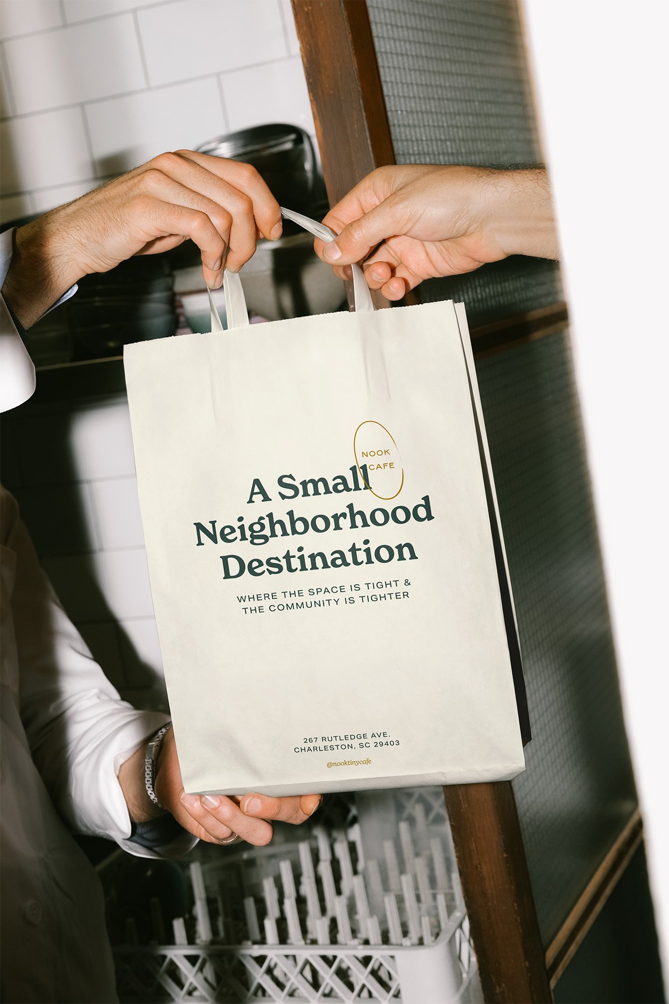 Person handing over a paper bag from Nook Cafe with the phrase "A Small Neighborhood Destination" printed on it.