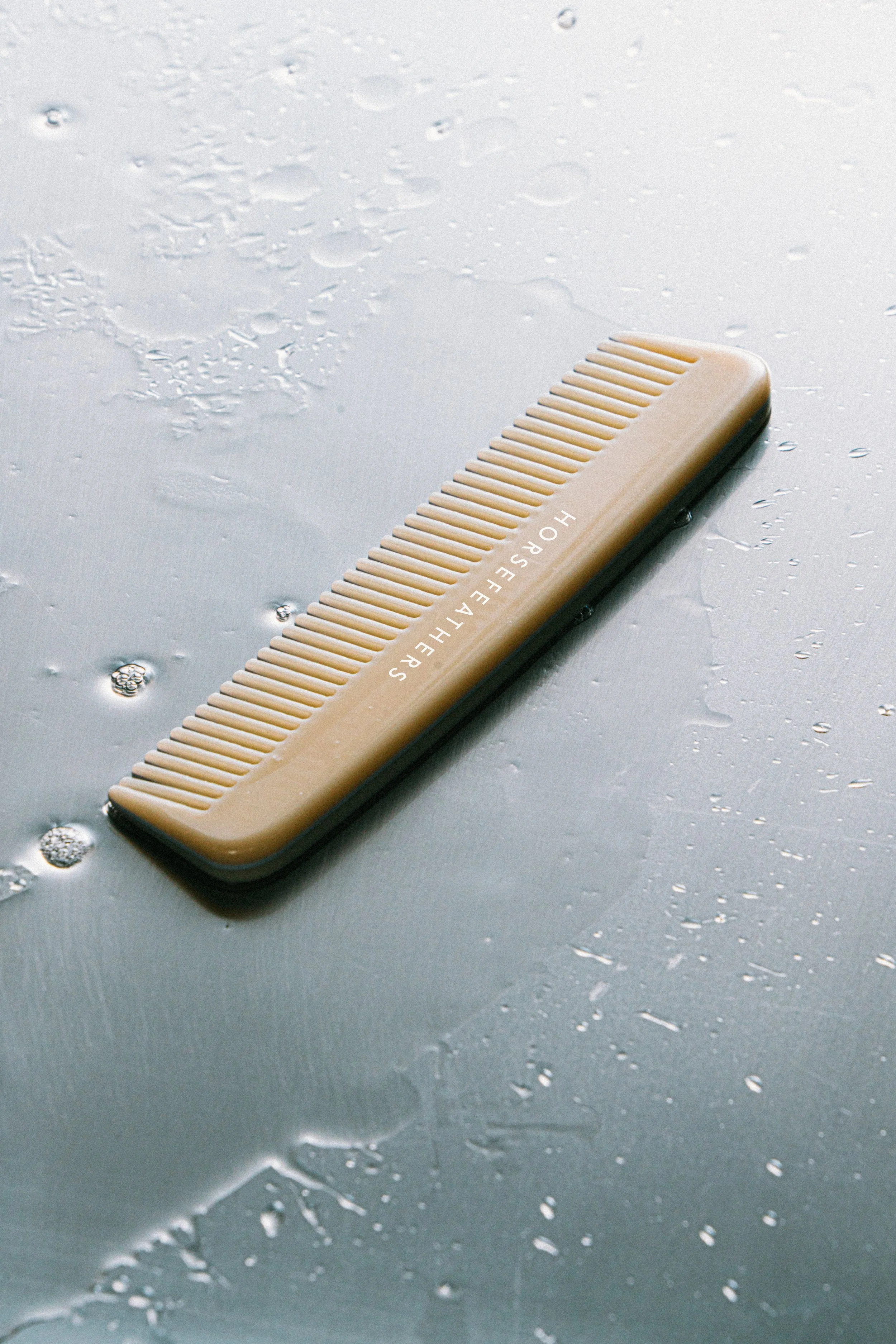 A beige hair comb labeled 'HORSEAFIELDERS' on a wet, reflective surface with water droplets.