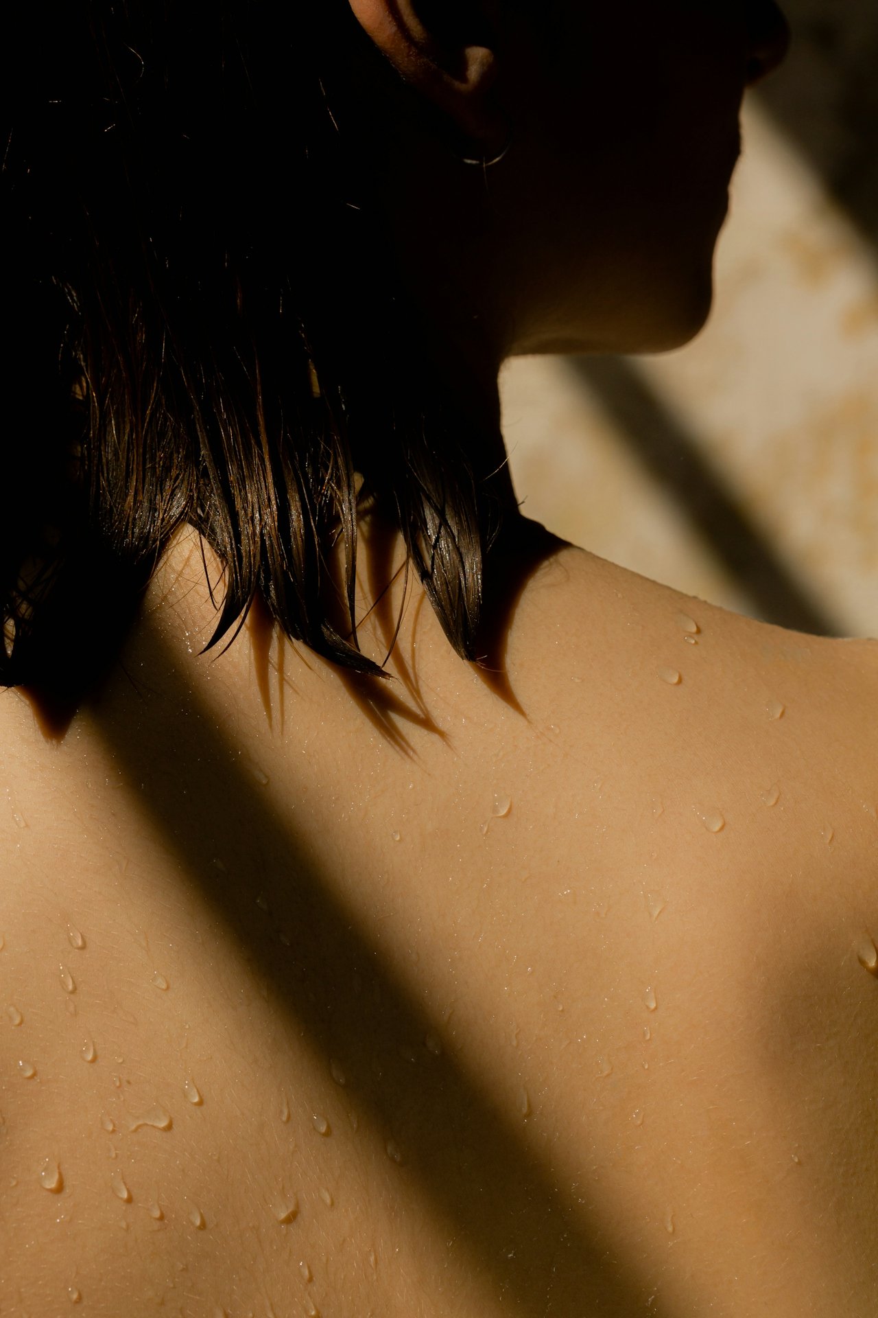 Close-up of a woman's shoulder and neck with water droplets, with her face partially visible and wet hair hanging down.