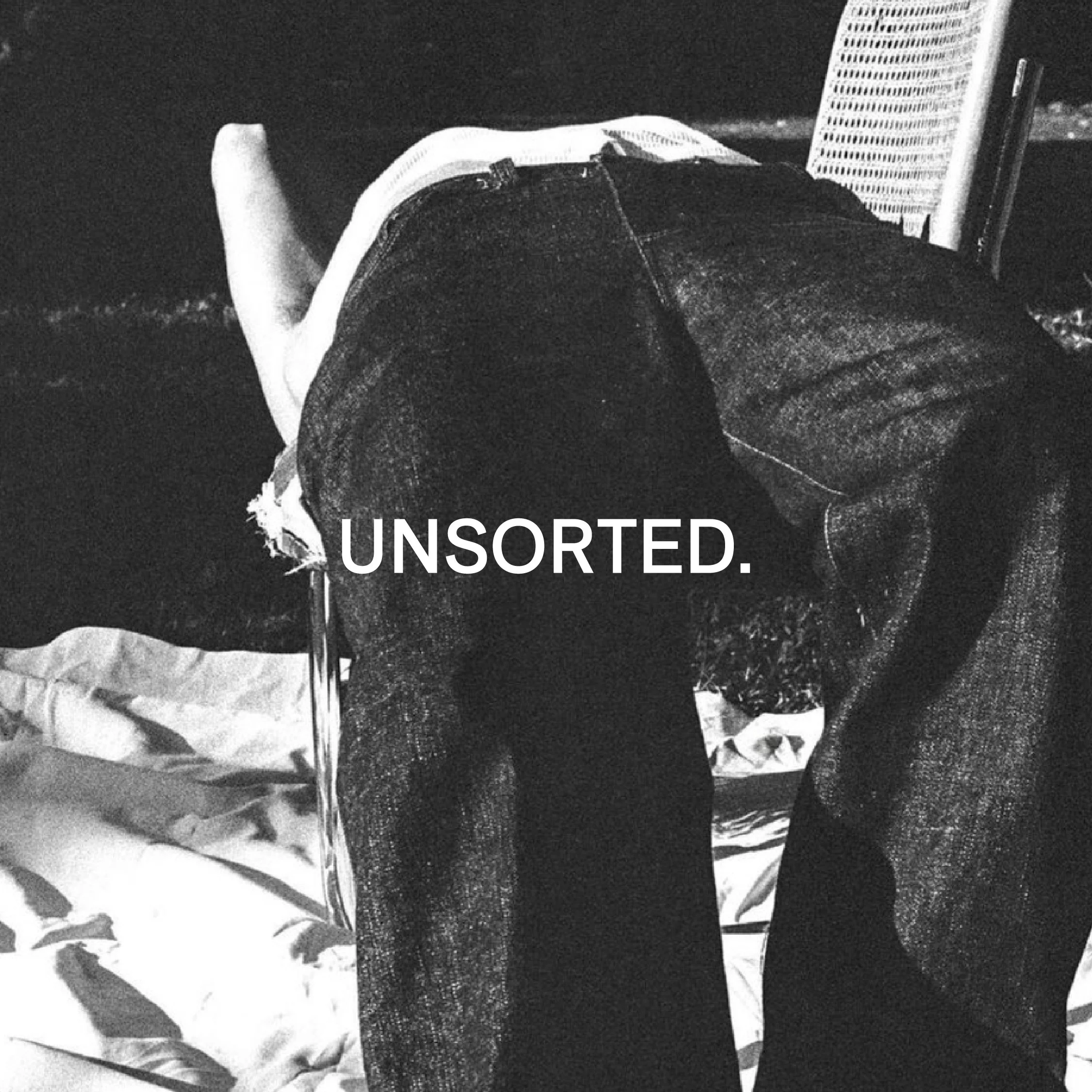 Black and white photo of a person wearing jeans, reclining on a chair outdoors with a caption saying 'UNSORTED.'