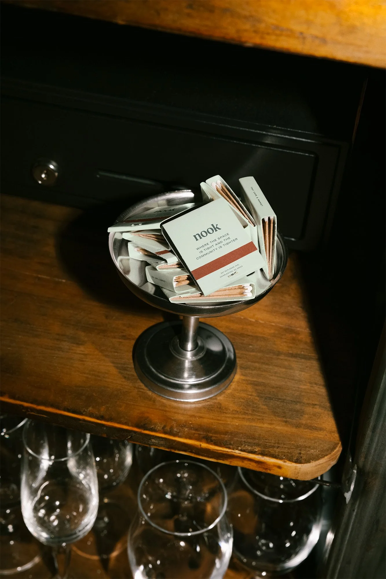 A small black dish filled with promotional cards labeled 'nook' on a wooden shelf, with glasses below.