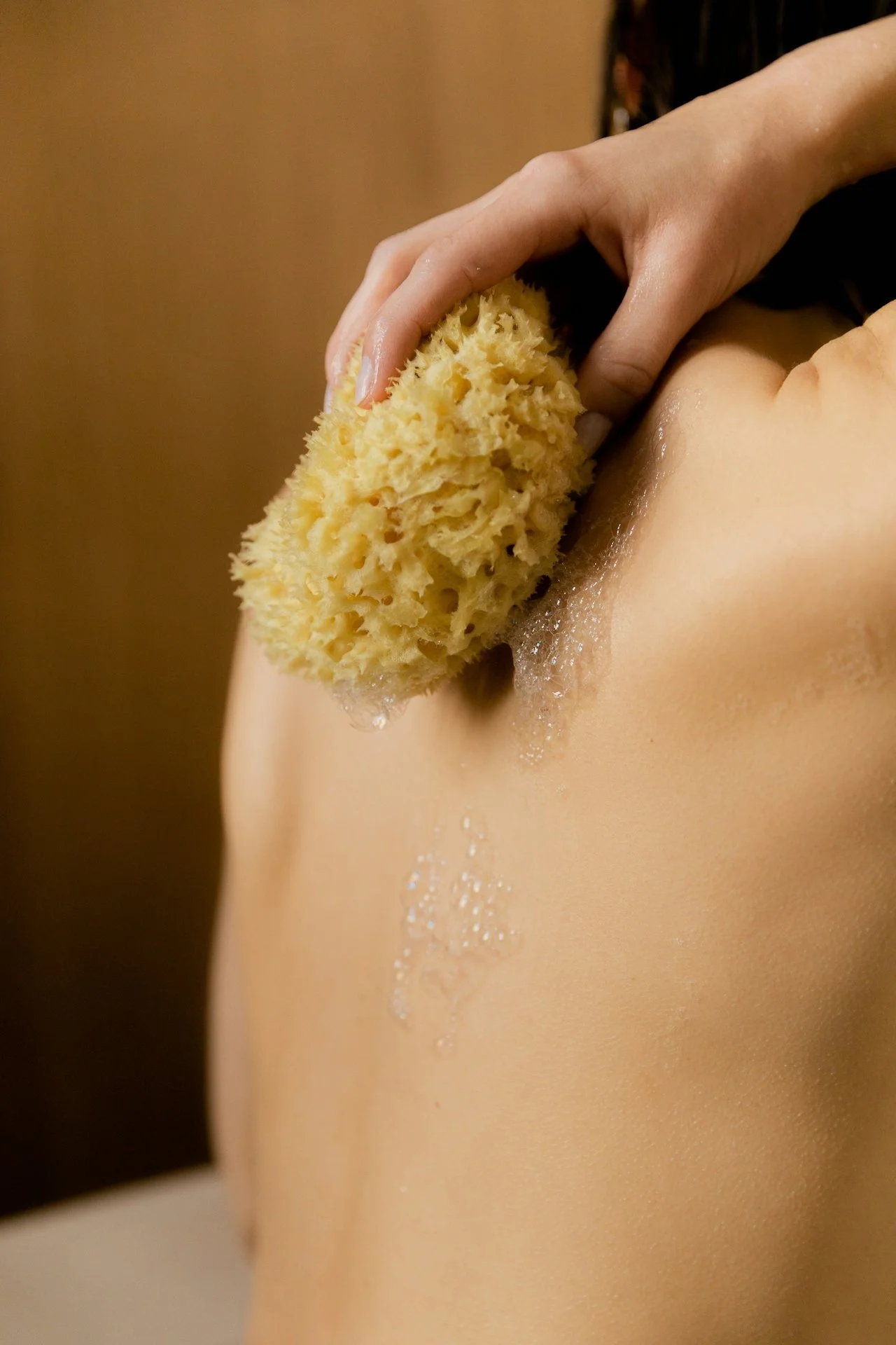 Close-up of a person's back being washed with a natural sea sponge, creating soap bubbles.