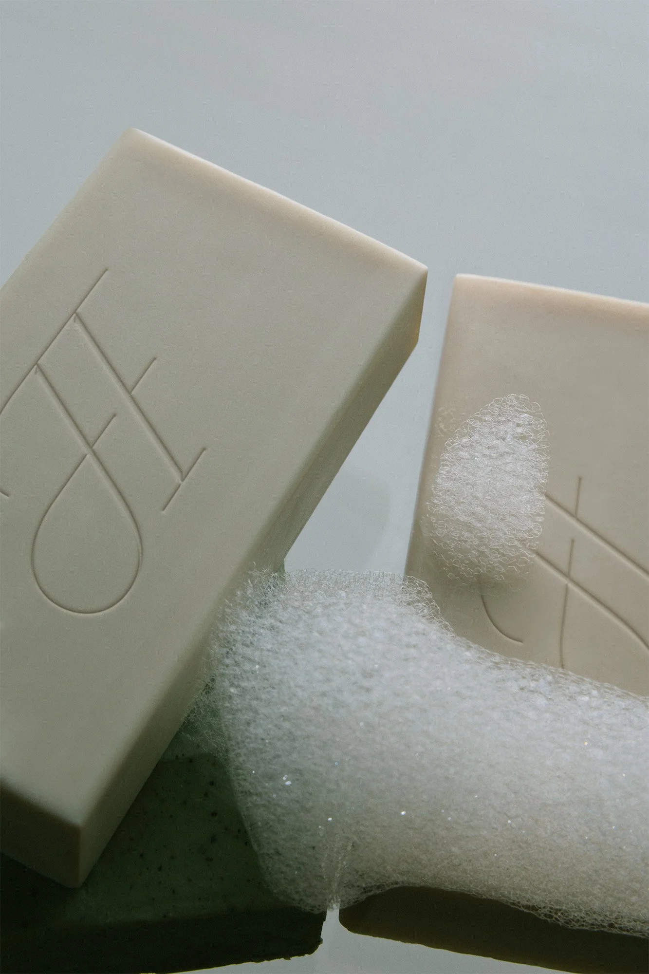 A bar of soap with the words 'THE' engraved on it, a piece of foam soap, and another soap bar, set against a light background.