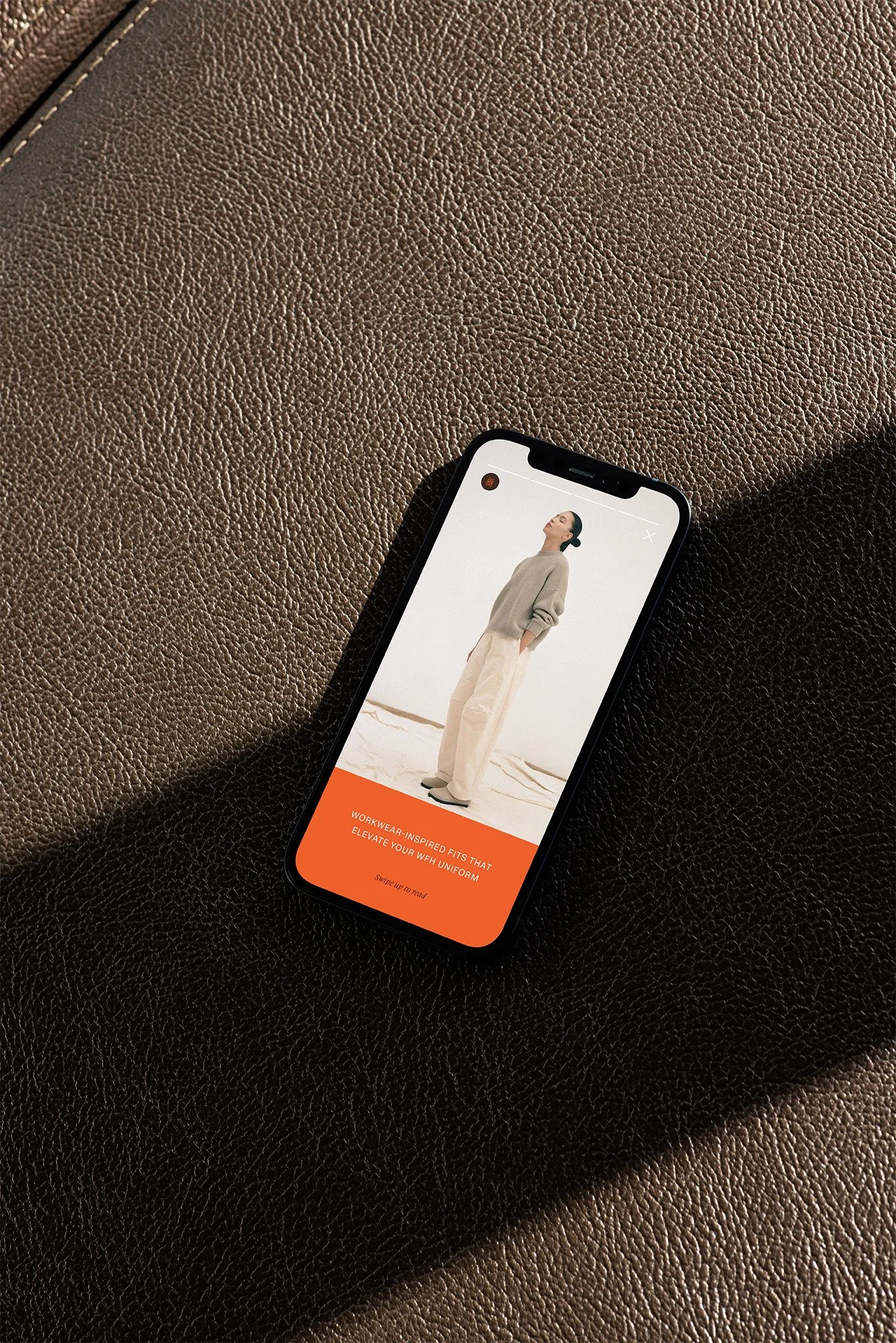 Smartphone displaying a website with a woman in neutral-colored clothing, standing in an outdoor setting, and orange text box at the bottom promoting workwear-inspired fashion.