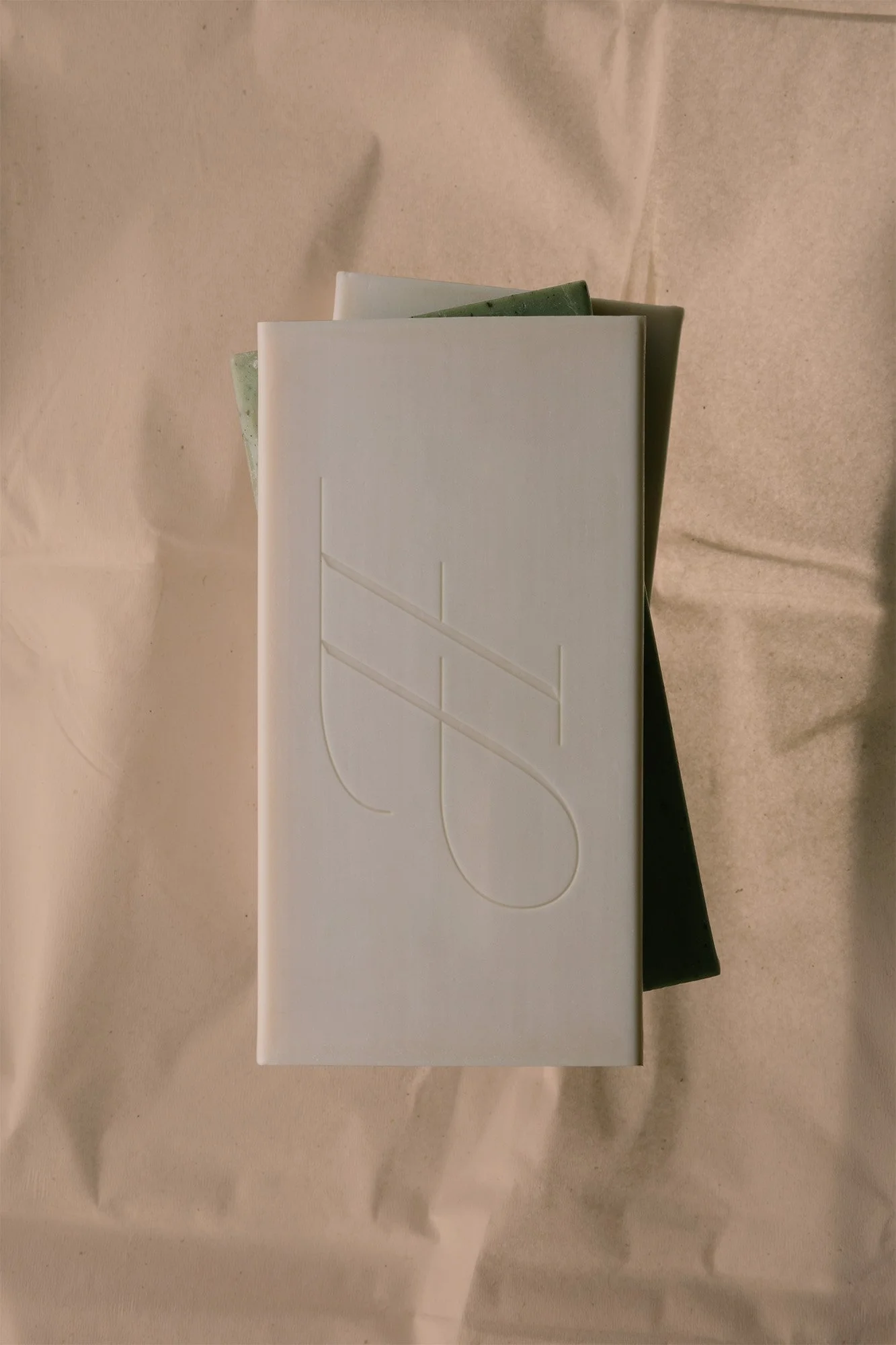 A white rectangular box with an engraved design on the top, placed on top of a slightly opened larger black box, with a piece of light brown wrapping paper underneath.