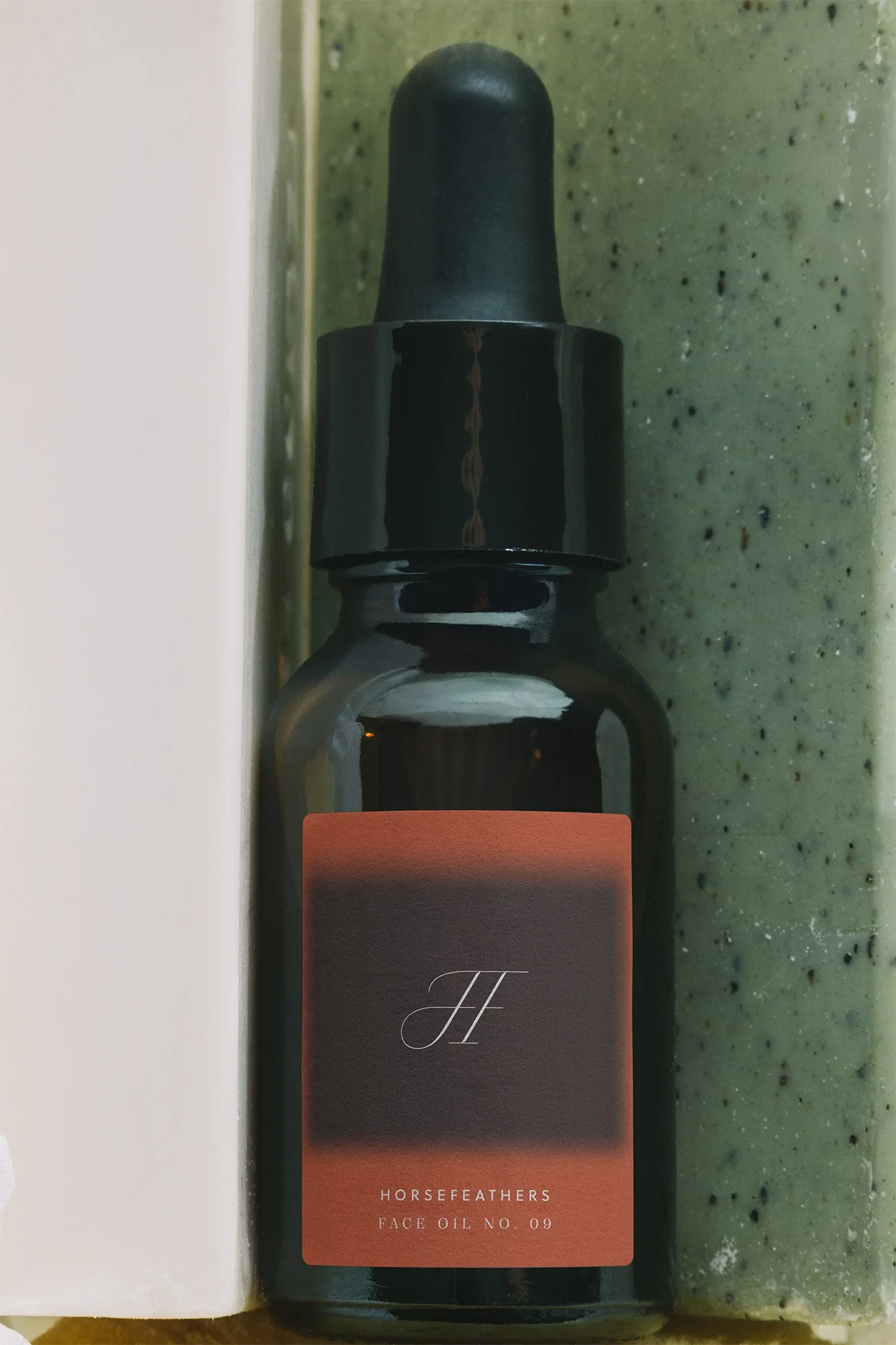 A dark glass bottle of Horse Feather Face Oil No. 09 with a black dropper cap standing on a green speckled surface.