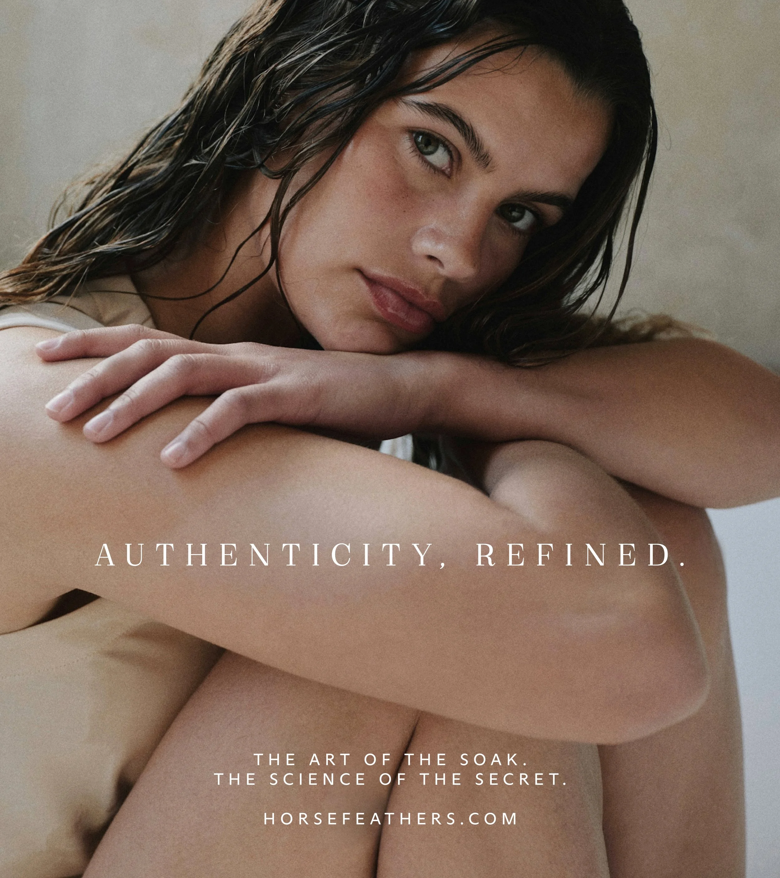 Close-up of a young woman with wet hair, resting her head on her knee, looking confidently at the camera, with text overlay: 'Authenticity, Refined. The art of the soak. The science of the secret. horsefeathers.com'.
