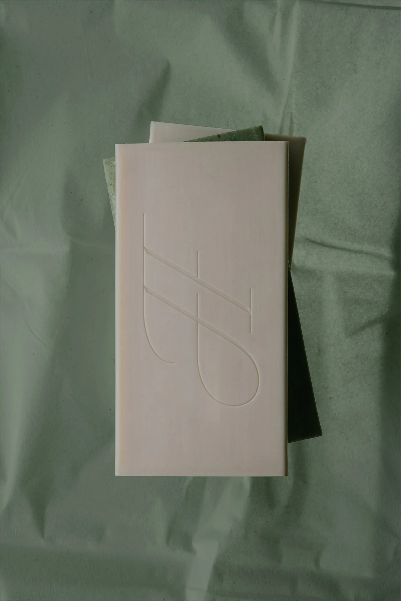 Stacked rectangular bars of soap, with pronounced embossing on the top bar, on a light green background.