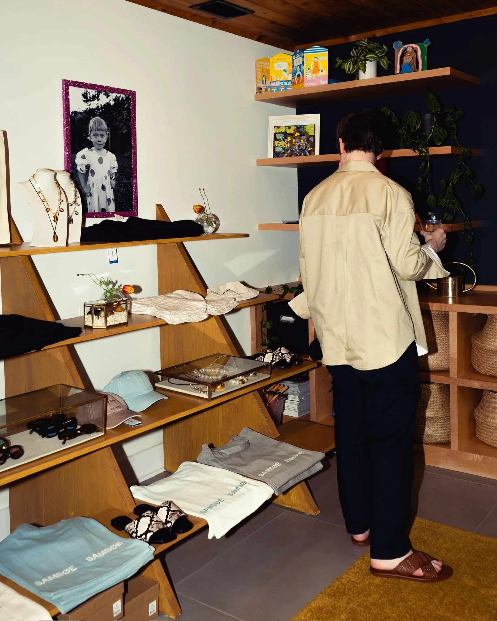 Person purchasing items in a boutique store featuring clothing, jewelry, hats, and accessories with framed artwork and shelves with decorative objects.