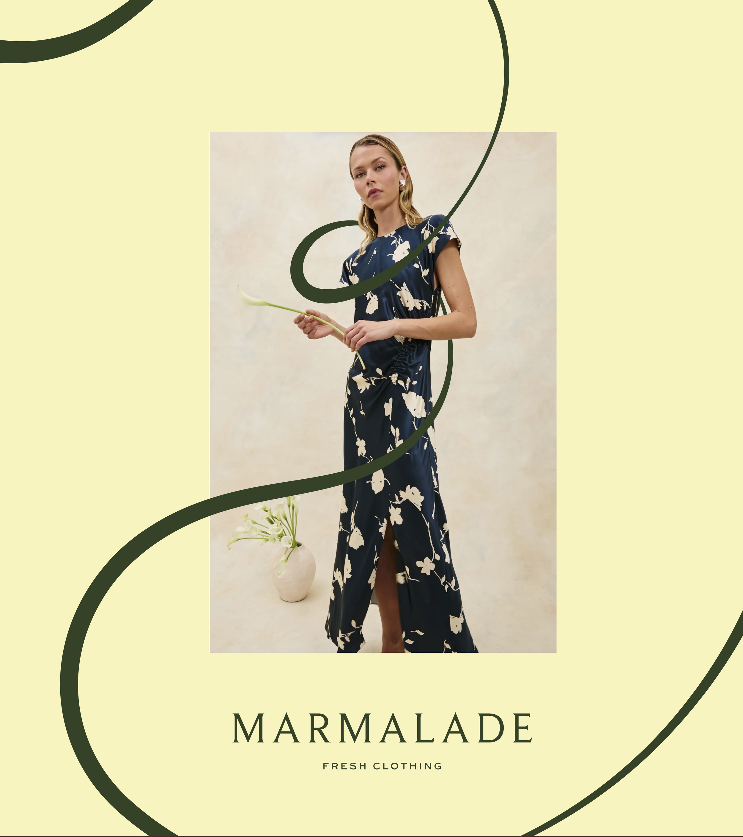 A woman wearing a navy blue floral dress holding a flower, standing in front of a neutral background, with a vase of white flowers on the floor beside her, and artistic green swirls in the foreground, promoting Marmalade Fresh Clothing.