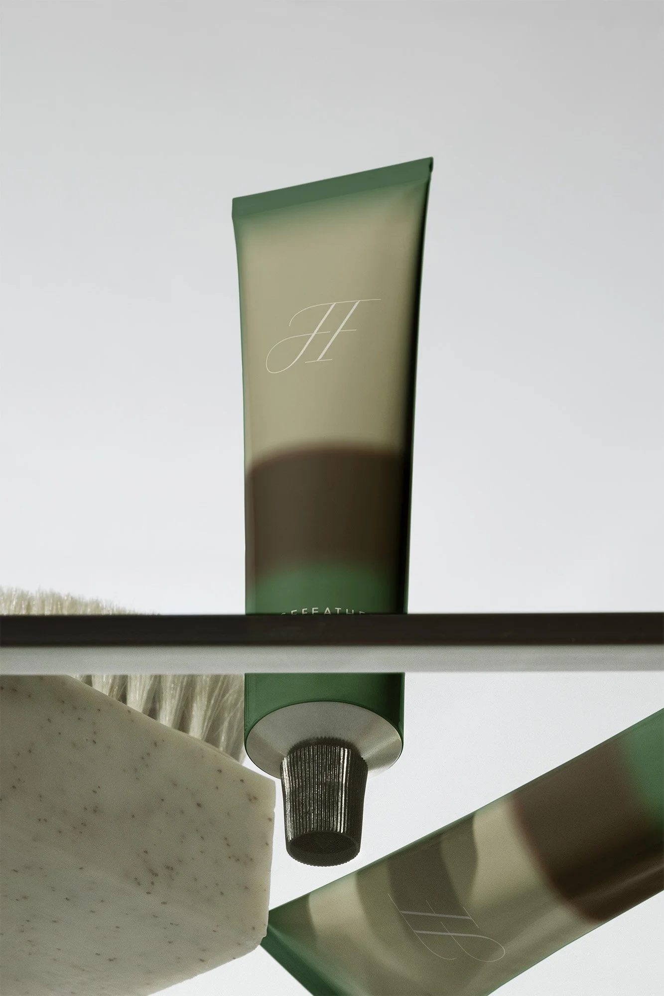 Close-up of a green exfoliating scrub tube, a green tube of cream, a black pump dispenser, a white exfoliating scrub bar, and a toothbrush on a shelf. The background is plain and light-colored.