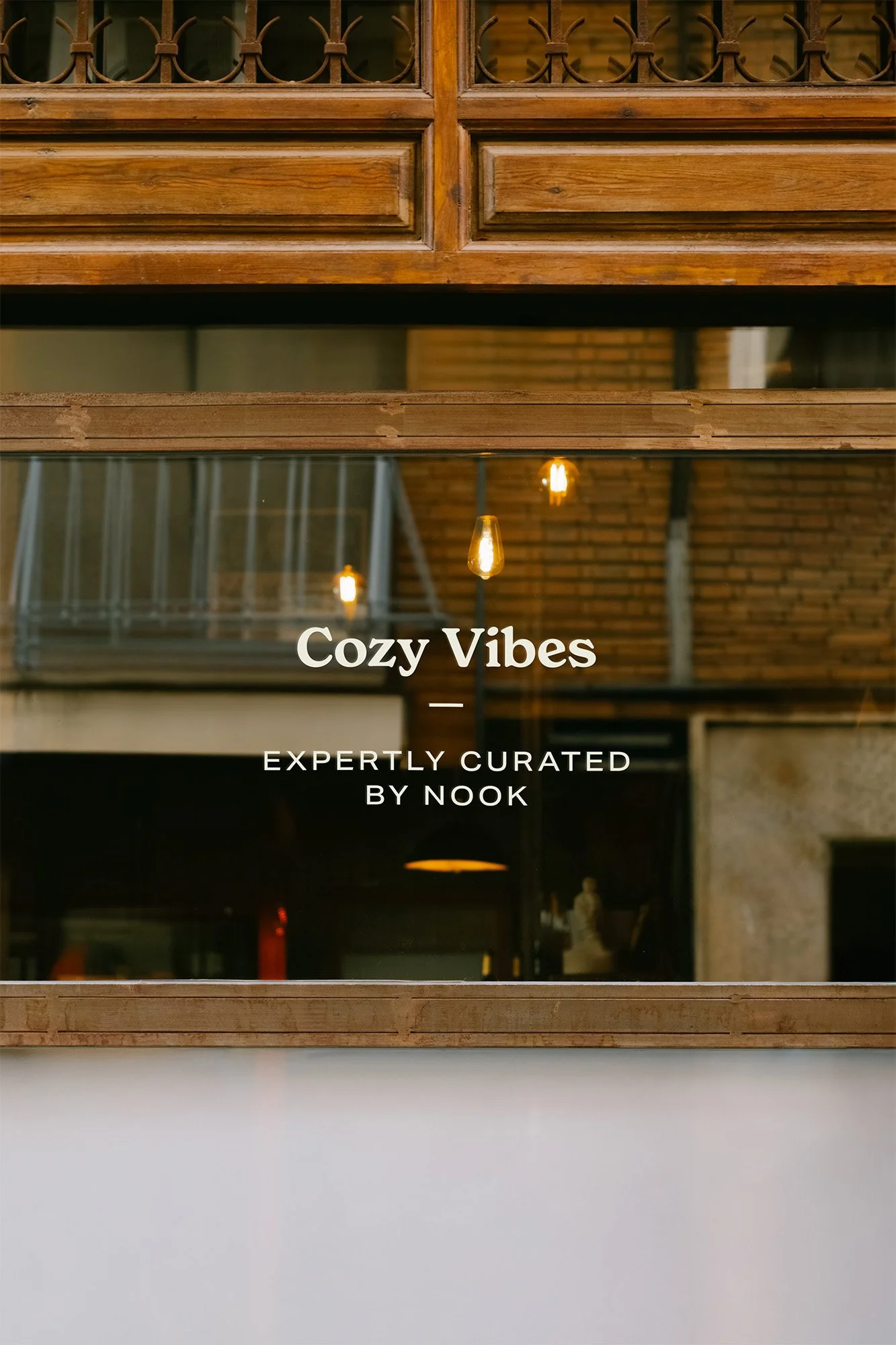 Reflective glass window with the words "Cozy Vibes - Expertly curated by Nook" displayed, wooden accents, warm lighting, and interior decor visible inside.