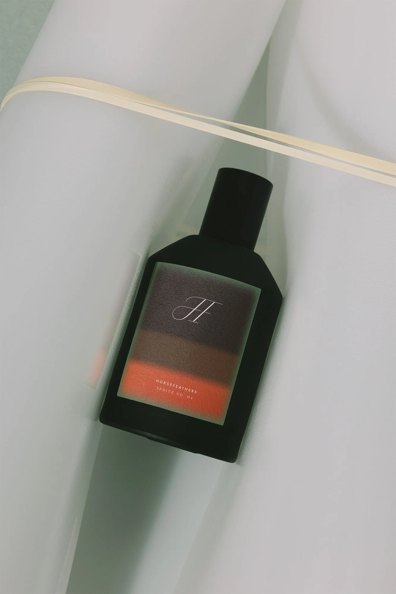 A black bottle with a minimalist label that reads 'H' and 'HORSEFEATHERS SPRITZ NO 01', placed on a white surface with a decorative curved edge.