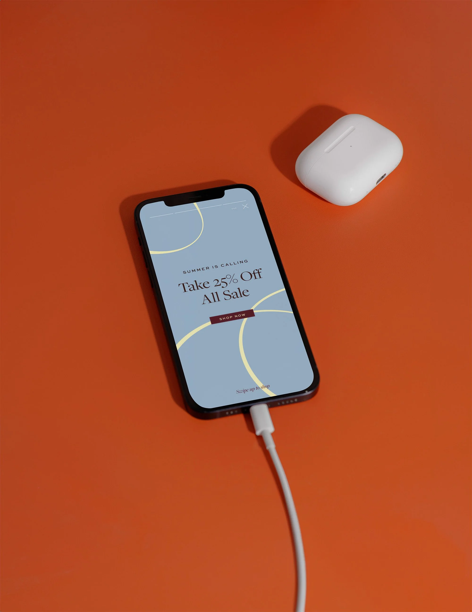 Smartphone displaying an online sale advertisement with a white charging cable connected, placed on an orange surface with a white wireless earbuds case nearby.