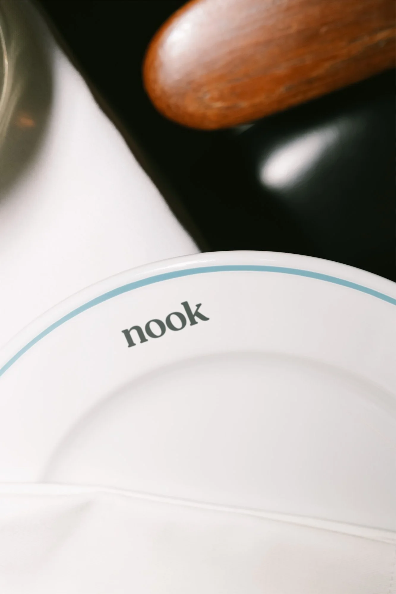 Close-up of a white plate with the word 'nook' printed on the rim, with part of a wooden chair and a black surface in the background.