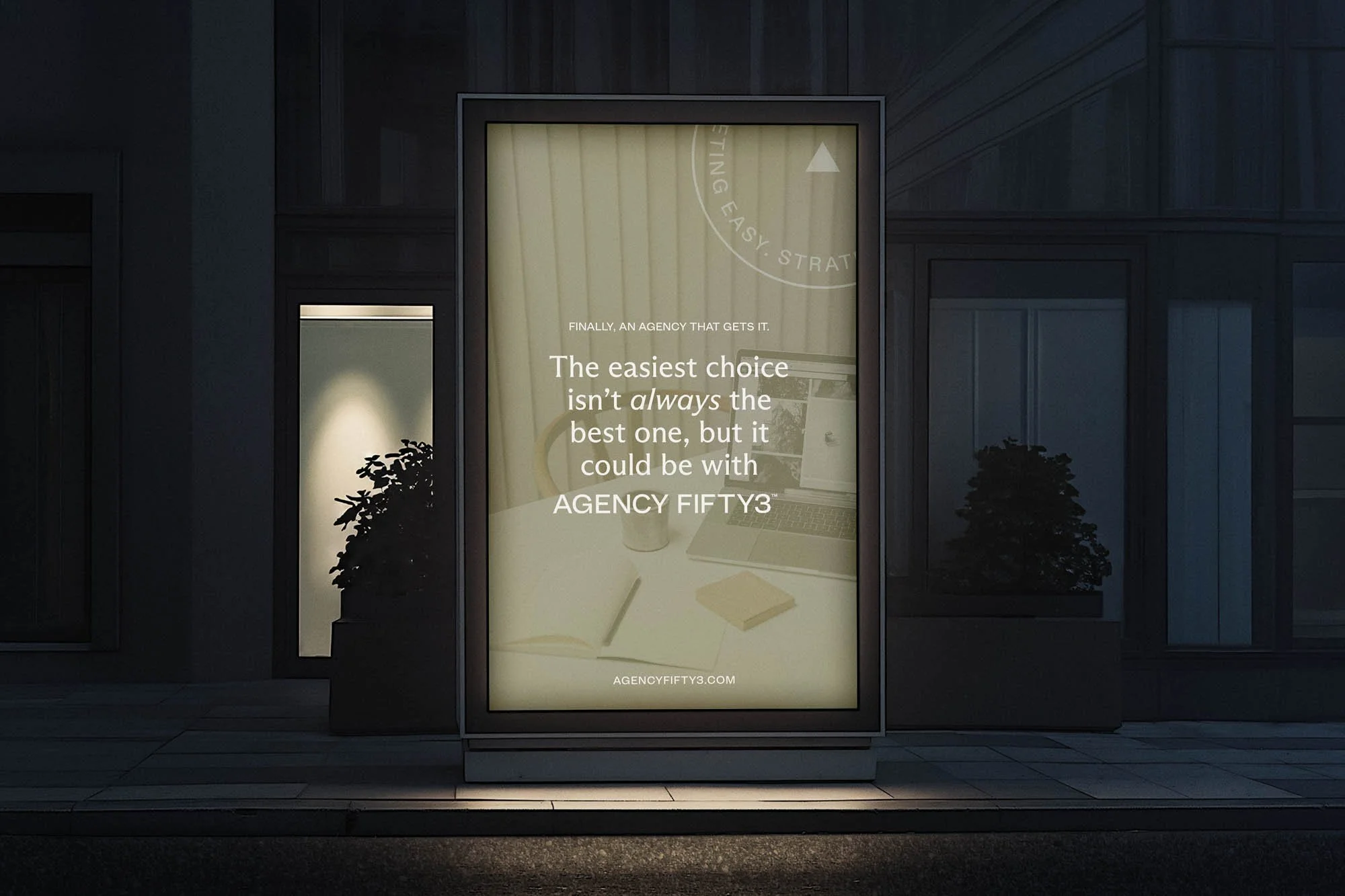 A backlit digital billboard on a city sidewalk displays an advertisement for an agency called AGENCY FIFTY3, featuring text about choosing the best agency.