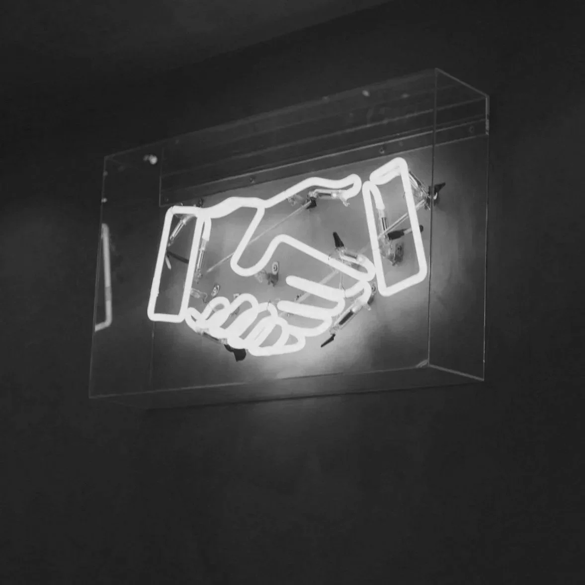 Neon sign depicting a handshake mounted on a wall.