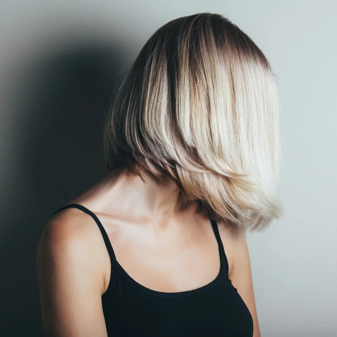 A woman with blonde, short, layered hair wearing a black tank top, facing away from the camera.