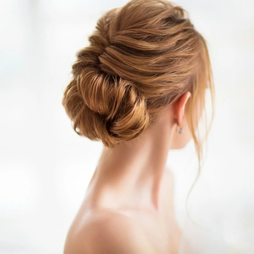 Back view of a woman with styled red hair in an elegant updo, identifiable by her shoulder and ear, with minimal background.