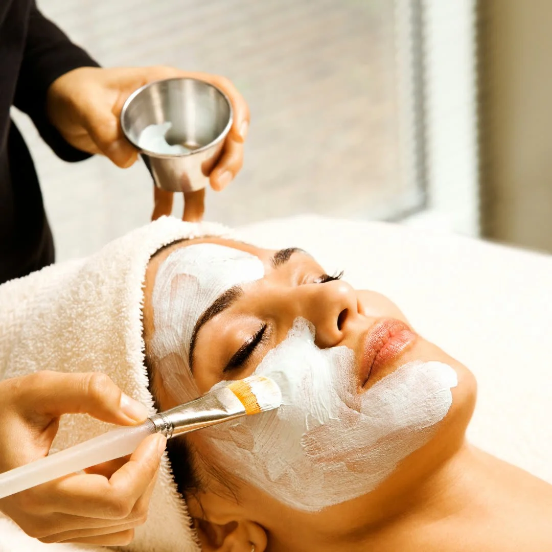 Woman receiving a facial treatment with a white cream applied to her face by a therapist in a spa setting.
