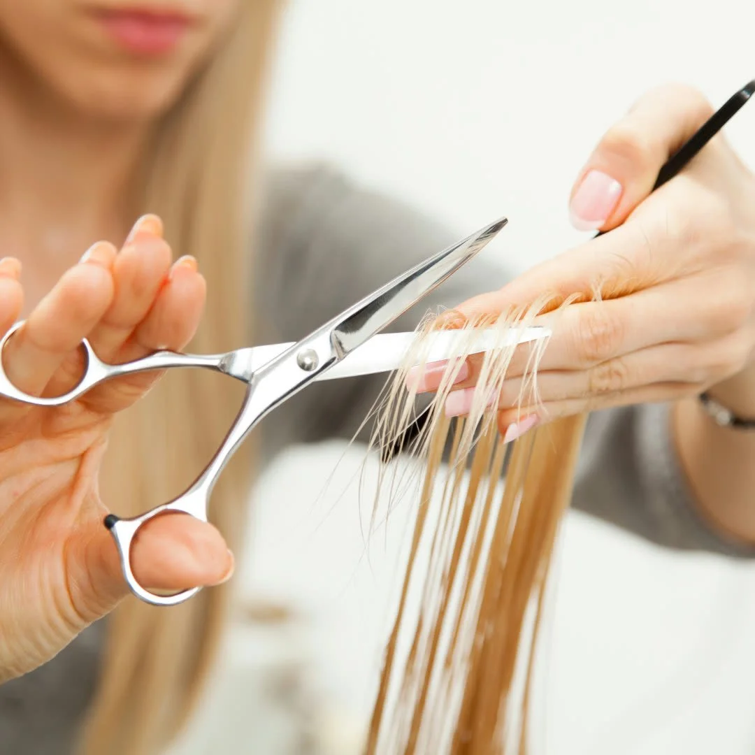 A person is slicing and trimming blonde hair with scissors and a razor.