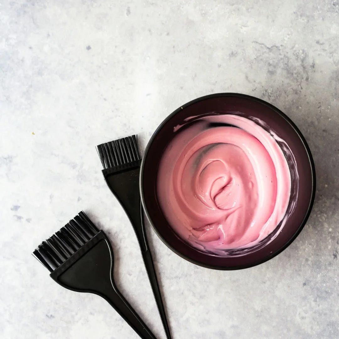 Black hair dye bowls and brushes on a light surface, with pink hair dye inside the bowls.