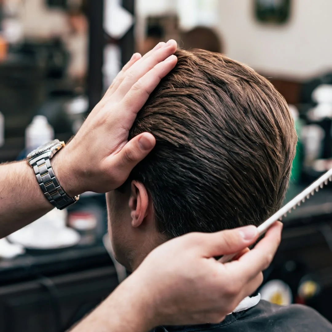 A person getting a haircut with a comb and scissors in a barbershop.