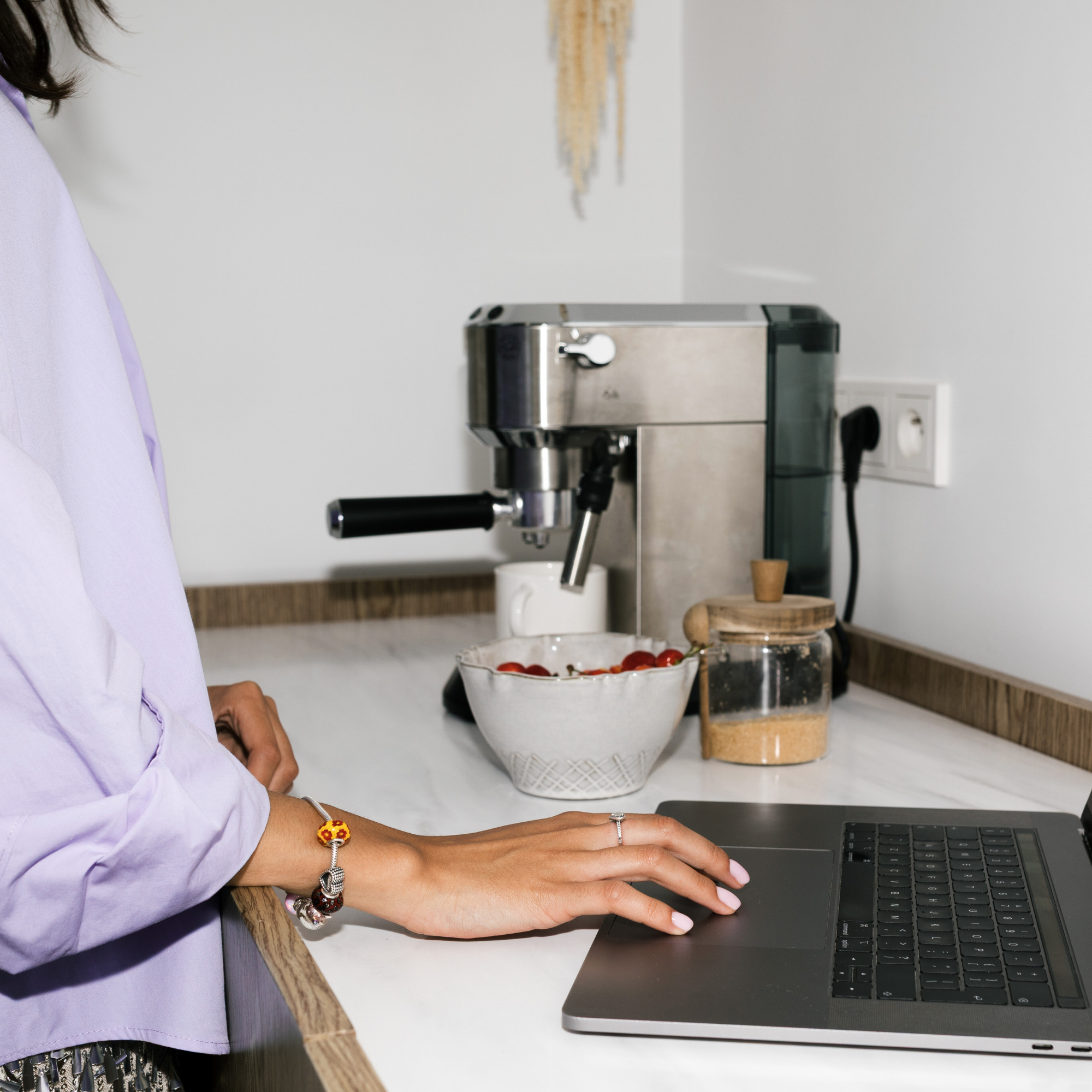 girl with pink nails making coffee and working on laptop