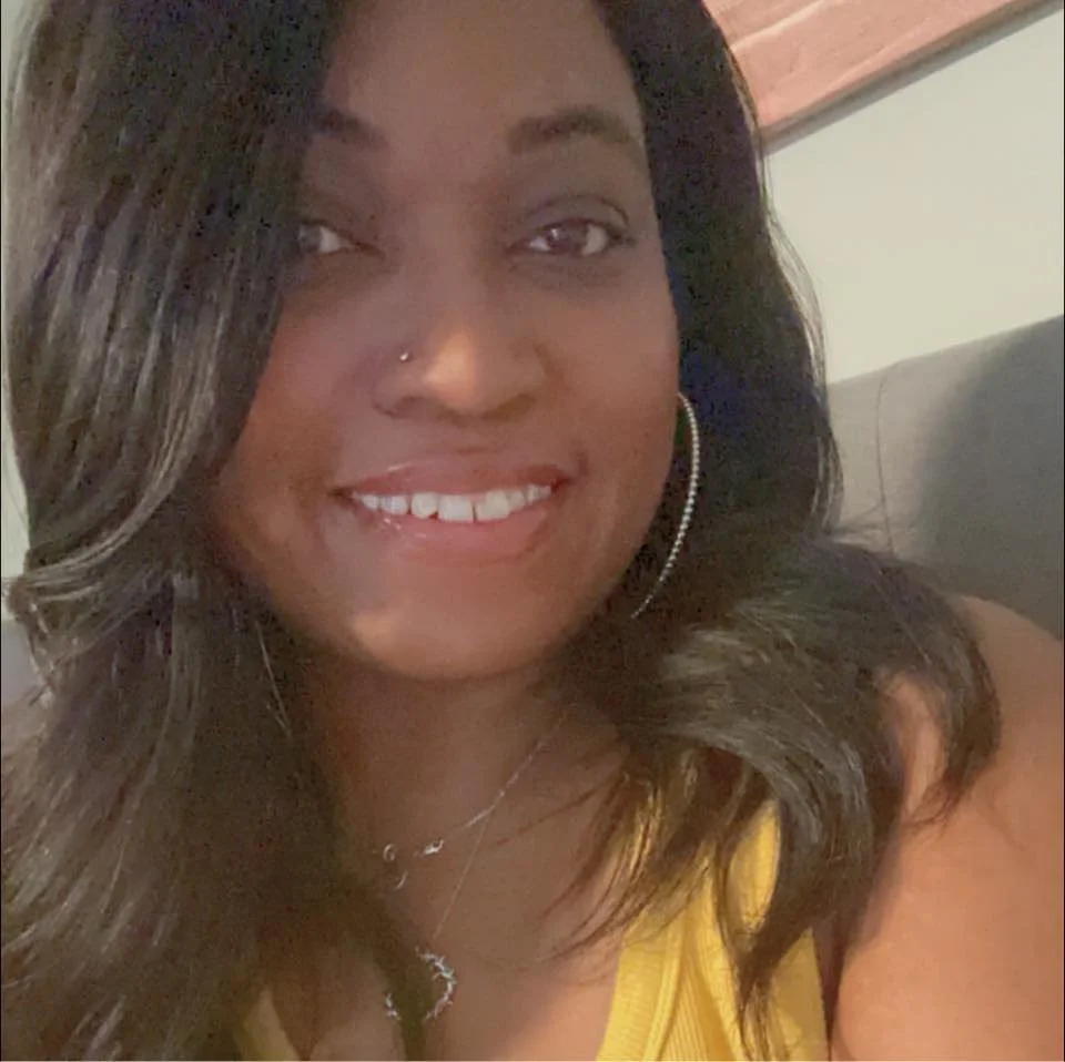 Smiling Columbus, OH Birth & Postpartum Doula Erica Lane with long hair and hoop earrings, wearing a yellow top.