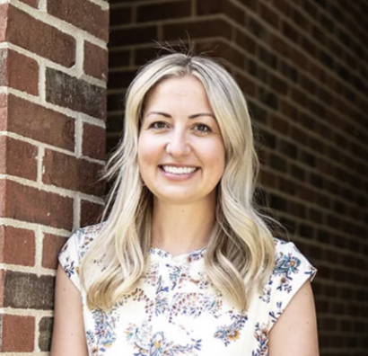 Amy Everhart Columbus, OH Mental Health Therapist with long blond hair standing against a brick wall, wearing a floral blouse.