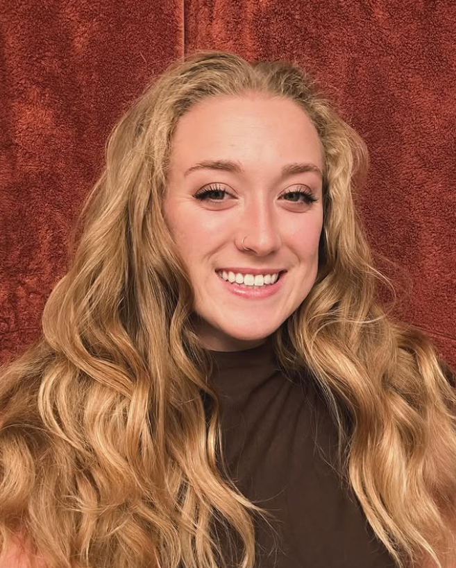 Columbus, OH Birth Doula Daisy Vance with long blonde hair smiling, wearing a brown top, against a red textured background.