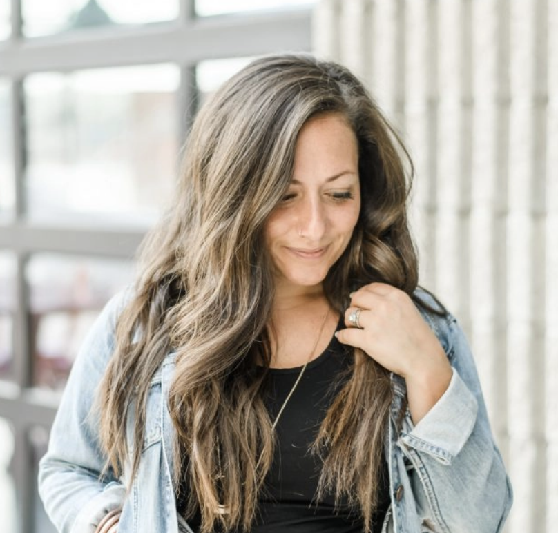 Fertility Nina Boyce with long hair wearing a denim jacket and black top, smiling gently while looking down.