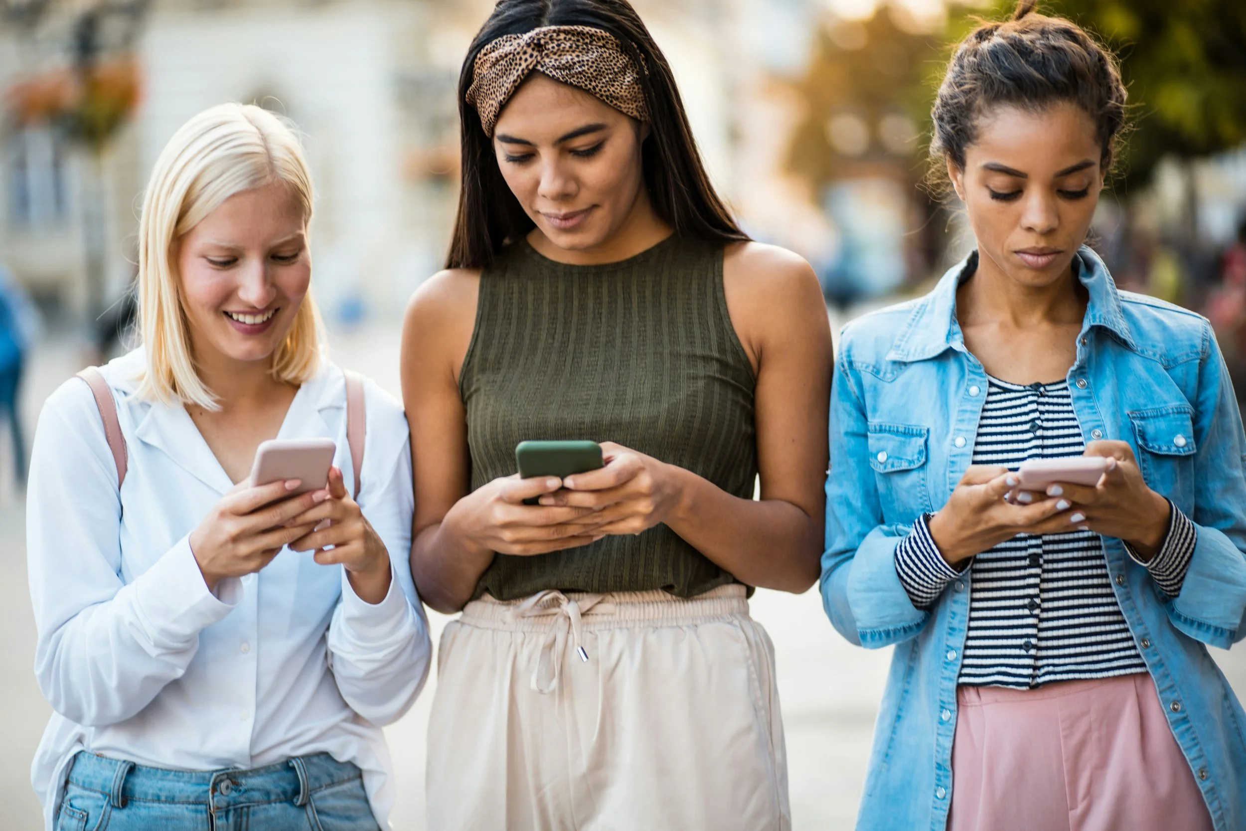 Three young women using smartphones together, representing social media influence on mental health awareness and self-diagnosis trends among Gen Z