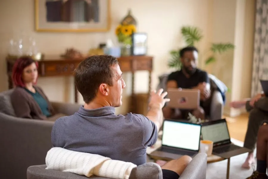 Group of therapists sitting together with laptops, talking and collaborating during a supervision or training session in a bright, modern workspace.