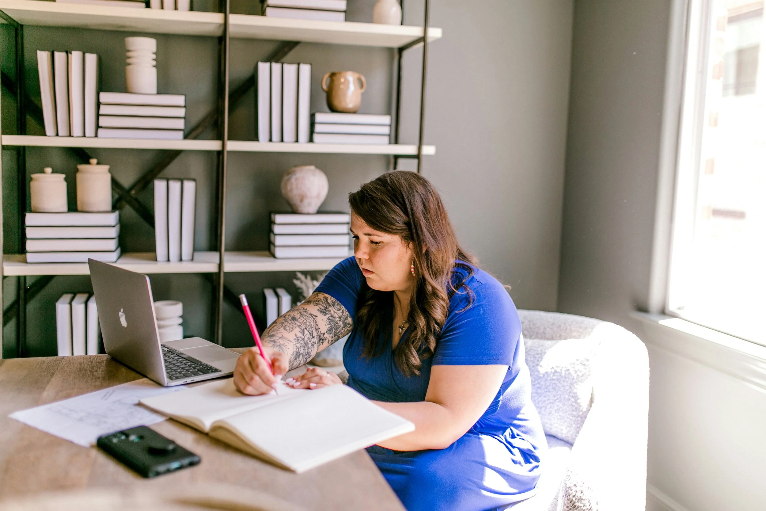 Therapist writing clinical notes at a desk beside a notebook and laptop.