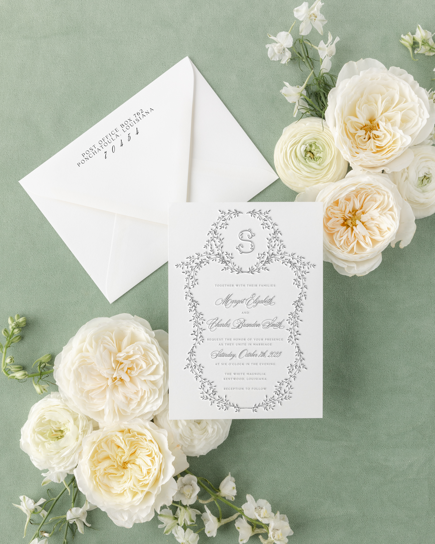 Elegant wedding invitation surrounded by white and cream flowers on a green fabric background