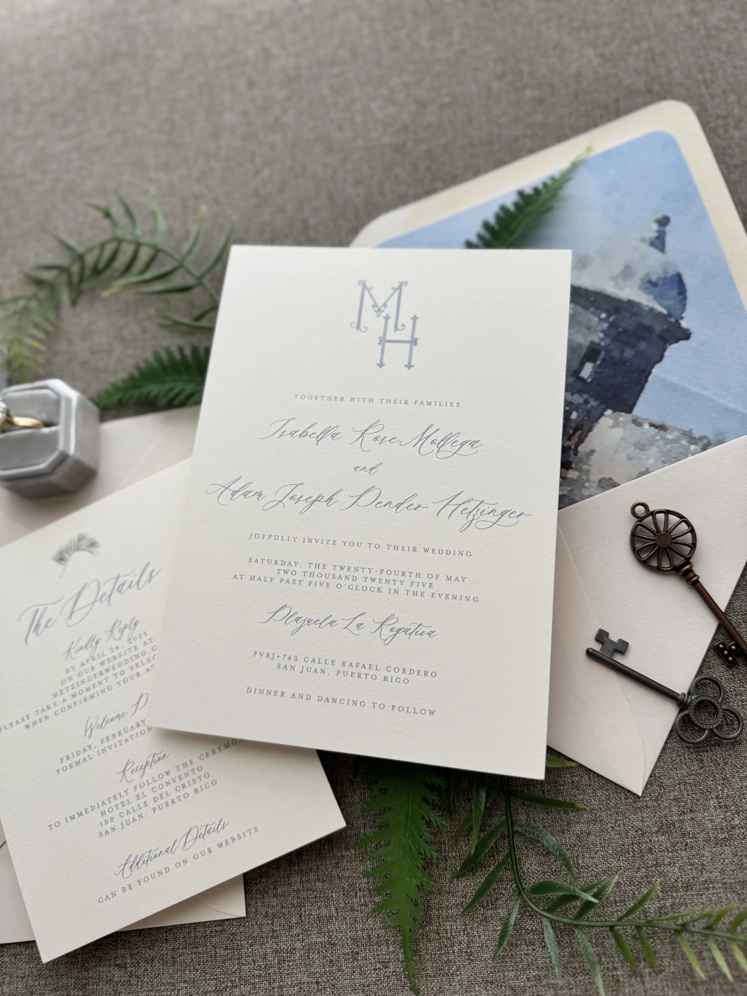 Wedding invitation with monogram initials 'M H', surrounded by greenery, vintage keys, and a watercolor painting of a lighthouse.